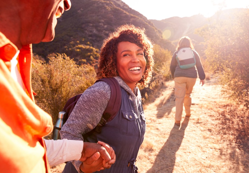 Two adults holding hands and smiling as they hike with another hiker ahead