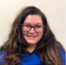 Female healthcare provider smiling and wearing black glasses and blue scrubs