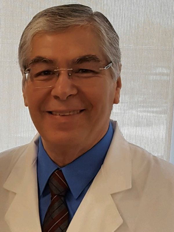 Male healthcare provider wearing a white lab coat, blue shirt, tie and glasses