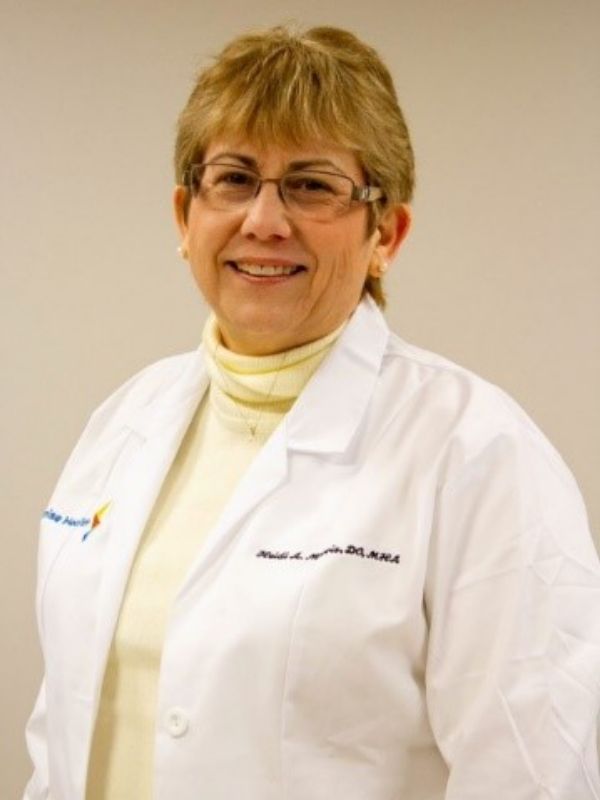 Smiling female healthcare provider wearing a white Premise Health lab coat and glasses